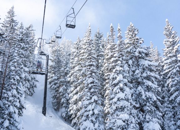 Snowy scenery depicting a chair lift going up the mountain between snowcapped pine trees at Park City Mountain.