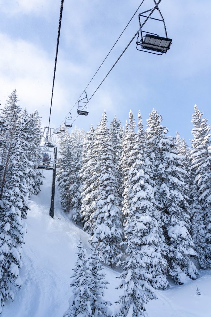 Snowy scenery depicting a chair lift going up the mountain between snowcapped pine trees at Park City Mountain.